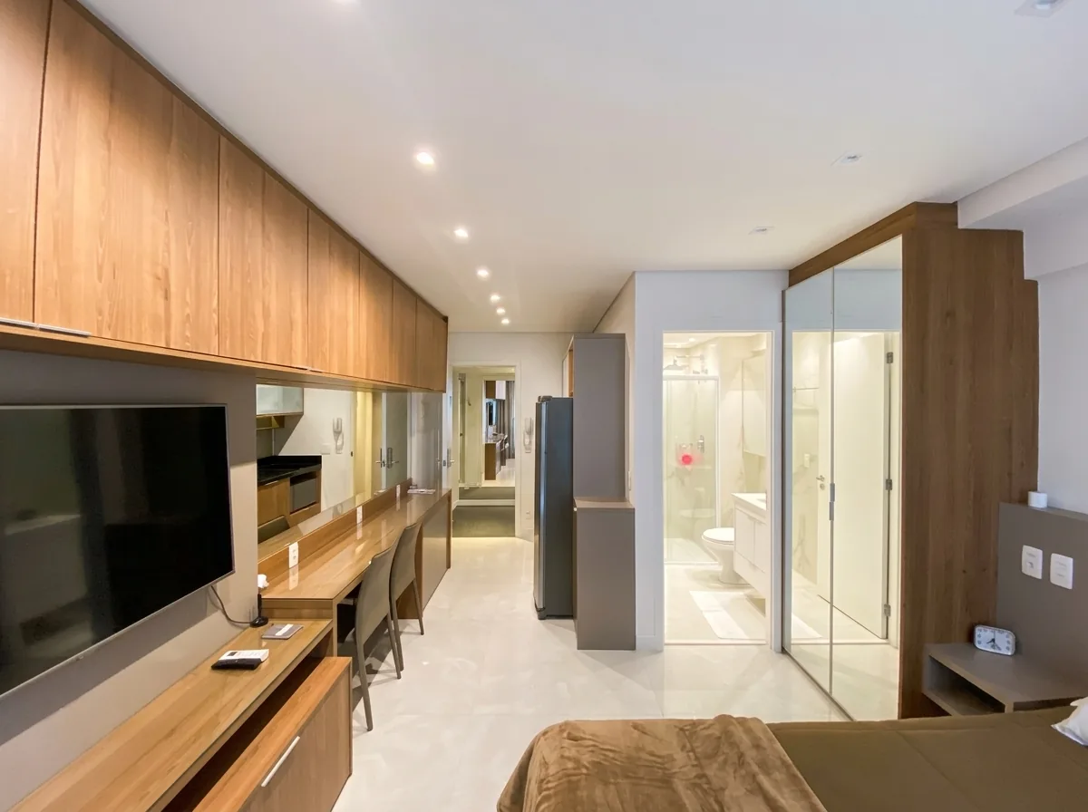 Dormitório com painel de TV em madeira, bancada de trabalho e closet com portas de vidro